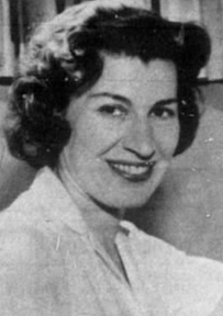 A smiling white woman with dark set hair; she is wearing a white blouse.