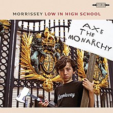 A young boy standing in front of the gates of Buckingham Palace. He is holding an axe in one hand and a sign saying "Axe the monarchy" in the other.