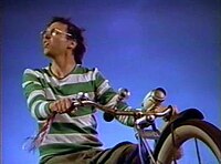 Neil Young as "Lionel Switch" riding a stationary bike against a surreal backdrop, an example of the film's "hyper-real sets." Humanhighwaystill02.jpg