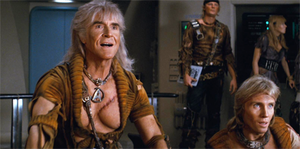 A film still showing Montalbán as Khan on the bridge of a spacecraft, wearing a torn golden shirt. His exposed chest bears a large scar, and his hair is long and grey. In the background, his followers wear similar clothes.