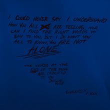 A handwritten message in dark text on a blue background. The message reads: "I could never say I understand how you all are feeling, nor can I find the right words to say to you, but I do want you all to know, you are not alone. The words at the end of this song are dedicated to you, Douglas High. Sincerely, XXX."