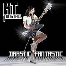 Tunstall stands against a black background wearing a white dress and heeled boots, facing to her left. She holds a glimmering guitar. Below her is the title "Drastic Fantastic" and in the top left, the name "KT Tunstall".