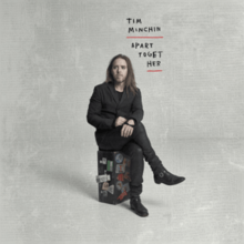 A man with long hair sits on a suitcase, with the words "Apart Together" written above him