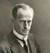 Man, mid-thirties, receding hair, clean shaven, wearing a high collar with tie. He is facing half right but his eyes are on the camera.