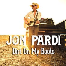 An image of a man playing a guitar on a dirt field with a pickup truck and sunlit background behind him. The artist's name and song title are colored in white and superimposed over the image.