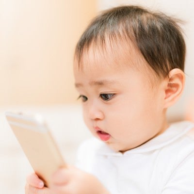 スマートフォンをおもちゃ代わりにする興味津々な赤ちゃんの写真