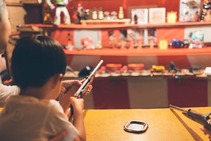 お祭りの出店にある射撃で銃を構える子供の写真