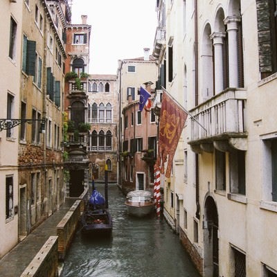 ヴェネツィアの水路に浮かぶ小船と旗が立つ建物（イタリア）の写真