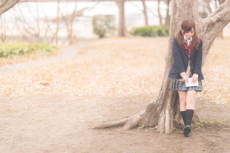 放課後、木陰に隠れて告白のチャンスを伺う女子高生の写真