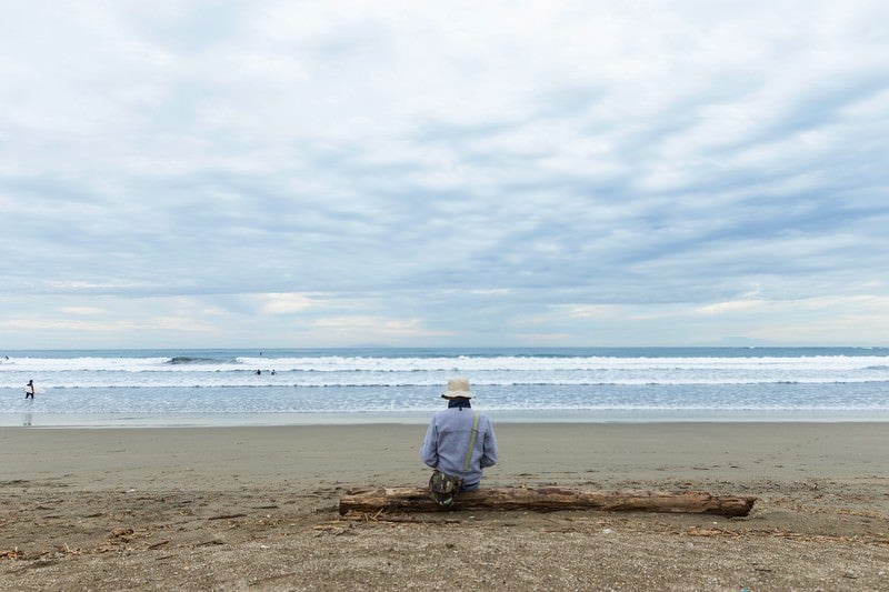 流木の上に座りサーファー達を見つめるエンジニアの写真