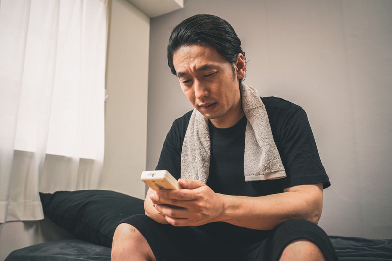 節電中、冷房をつけるか悩む男性の写真