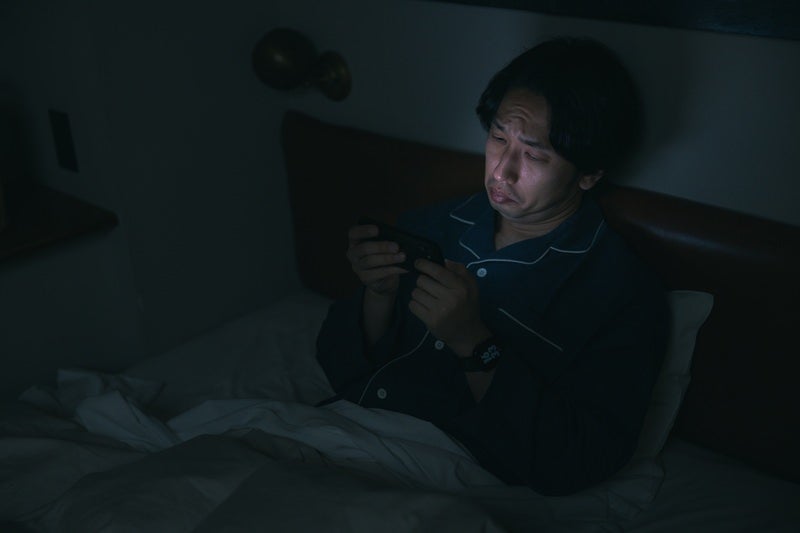 眠れなくてスマホで動画を見てしまう男性の写真