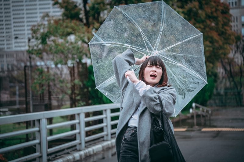 風に飛ばされそうな傘を持つ女性の写真