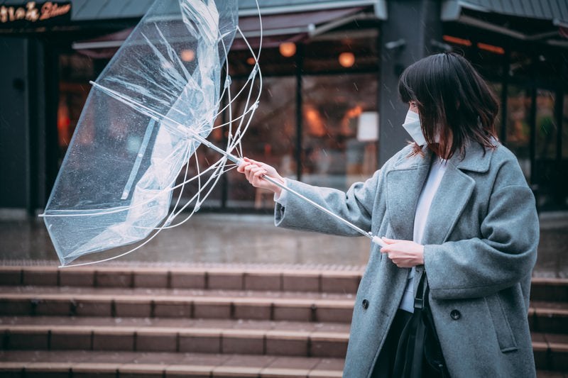 裏返ったビニール傘を元に戻す女性の写真