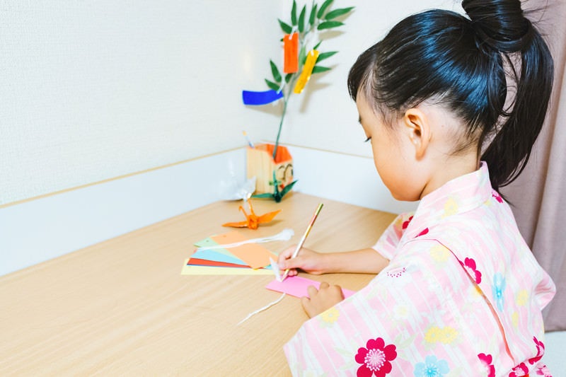 机の上で短冊に願いをこめる浴衣の女の子の写真