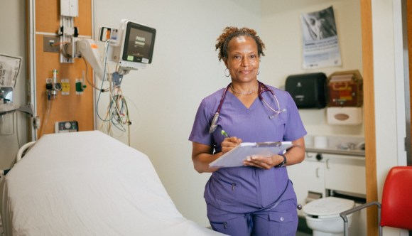 A VA nurse in an exam room, holding a clipboard.