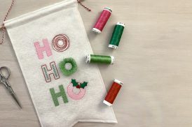 Machine embroidery design featuring stylized lettering spelling out the words, "Ho, Ho, Ho" using a mix of embroidery stitches in a mix of pink, red, bright green, and dark green.