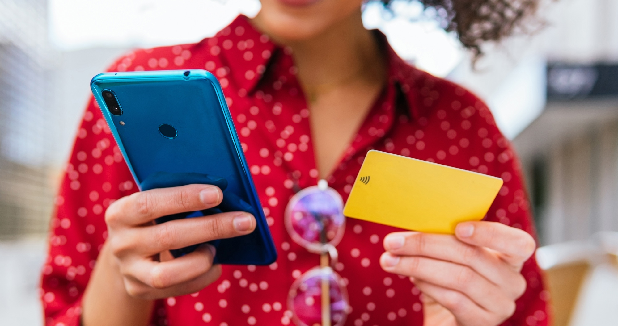 Person in a red shirt holding a blue cellphone and yellow card