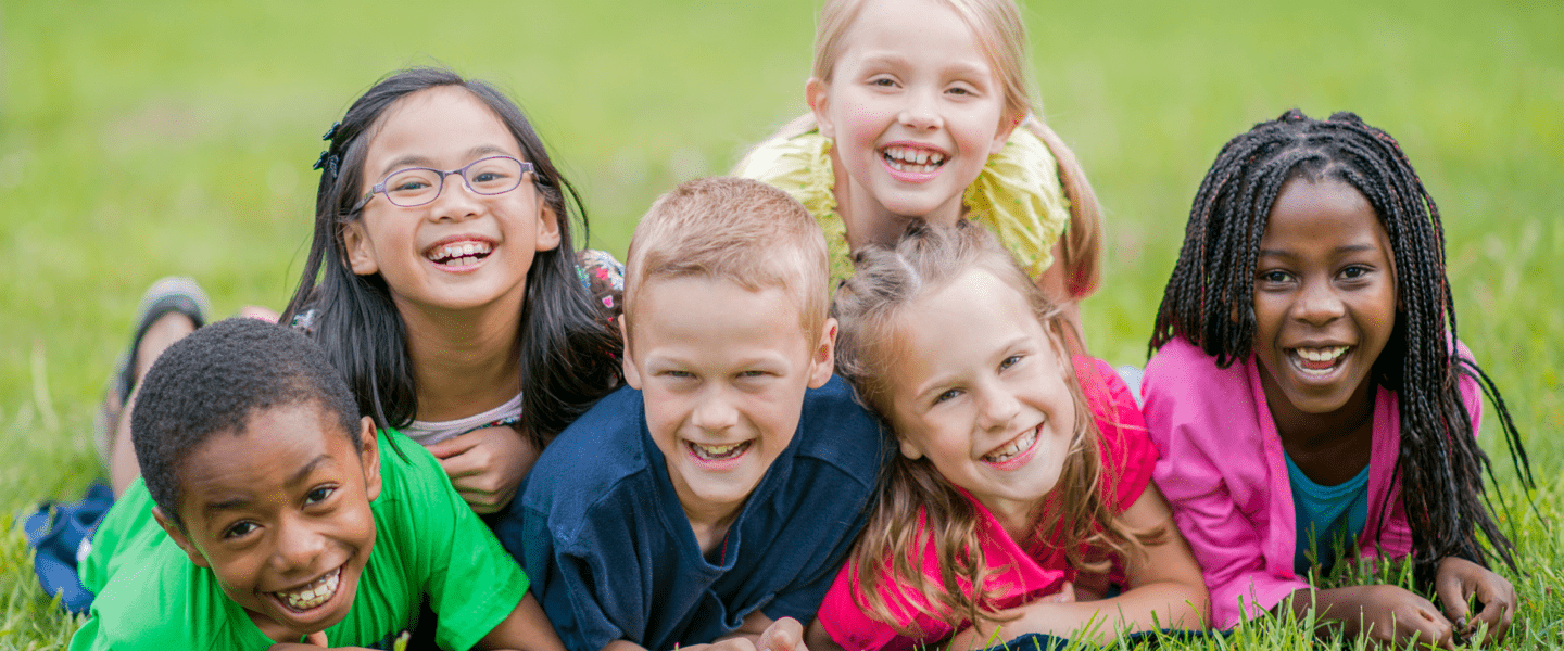 Diverse group of children smiling at the camera while lying in a field.