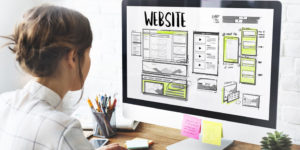 Business person designing a company website on her computer monitor that displays the heading ' Website' above webpage layouts and mock ups.