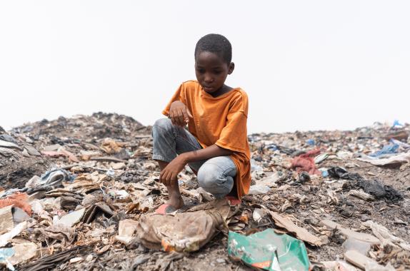 Photo: Child sitting on an African garbage dump, looking at the plastic waste.