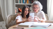 A granddaughter and grandmother look at a phone together.