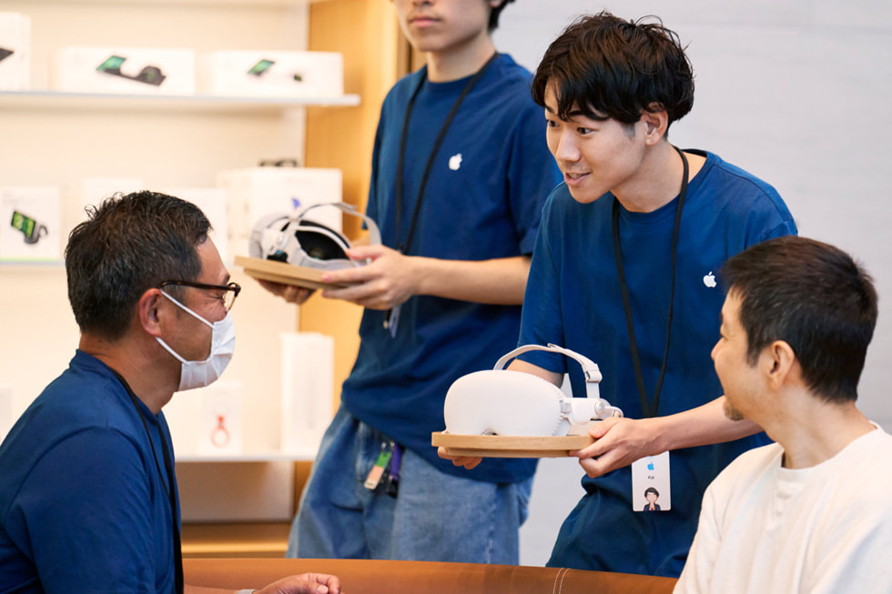 Los integrantes del equipo acercan dispositivos Apple Vision Pro a los clientes que esperan sentados en la zona de prueba.