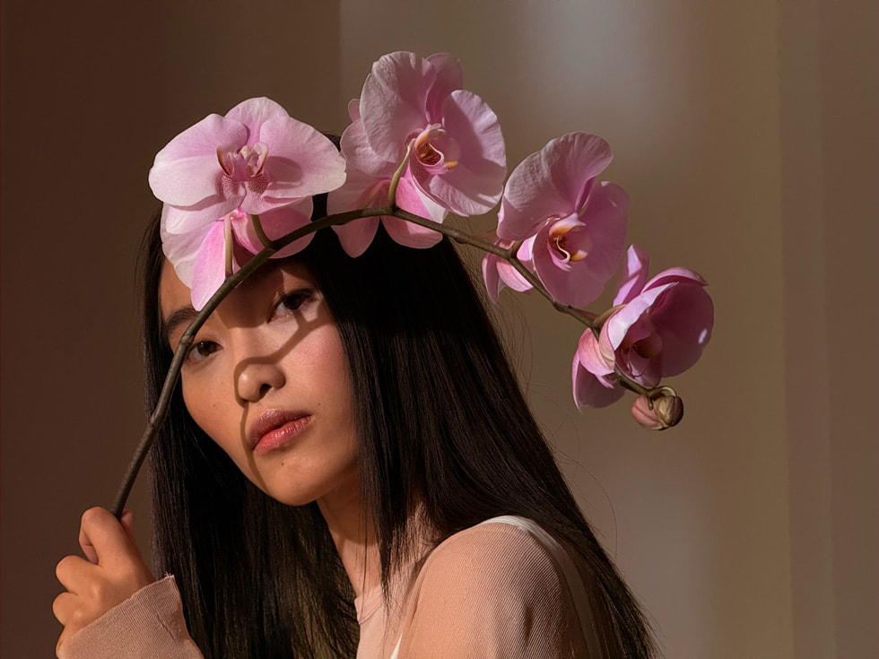 A person holds a pink orchid branch in an image shot on iPhone 16 Pro.