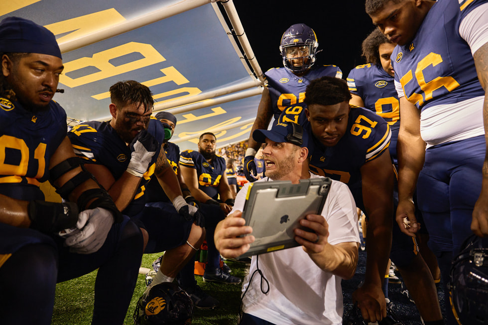 Cal players and coaching staff review iPad footage on the sideline during a football game.