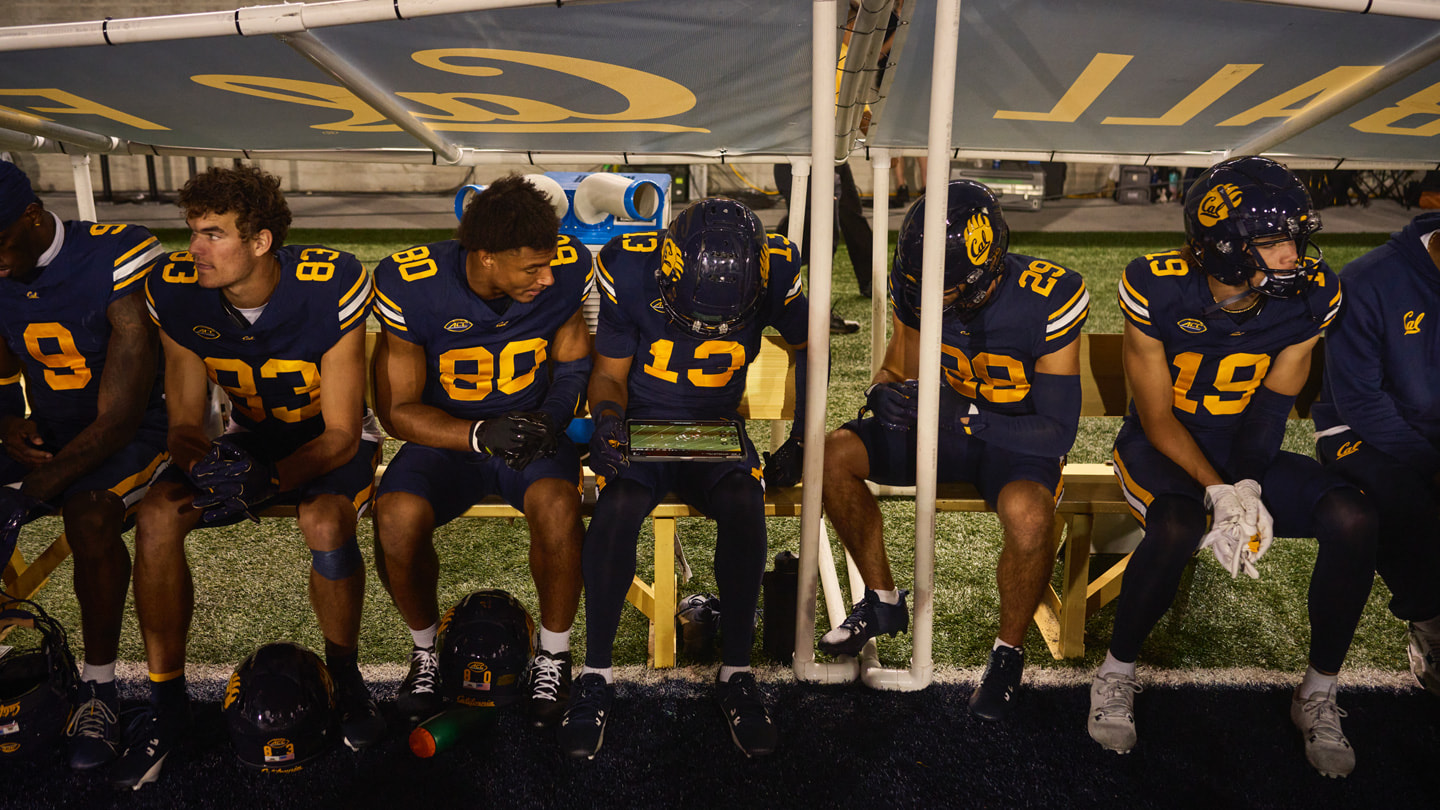 Cal teammates sit on the bench during a football game and review footage on iPad Pro.