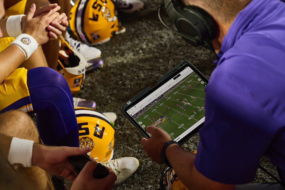 LSU coaching staff and players review footage on iPad Pro on the sideline of a football game.