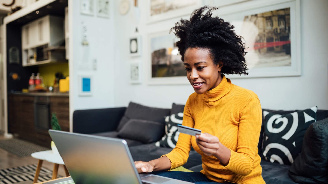 Young woman uses credit card snd laptop in living room