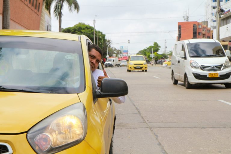 Taxista conduciendo y saludando con la cabeza por fuera y dedo arriba.