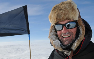 A man wearing cold weather clothing in front of a marker flag on the ice