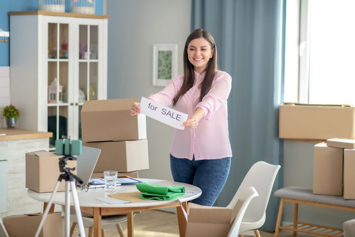 Recording a video. Dark-haired young woman holding a table for sale before the camera