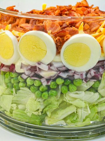 This easy 7-layer salad recipe is a crowd-pleaser with crisp romaine, peas, onions, bacon, eggs, cheese, and creamy dressing. Perfect for potlucks or make-ahead meals!