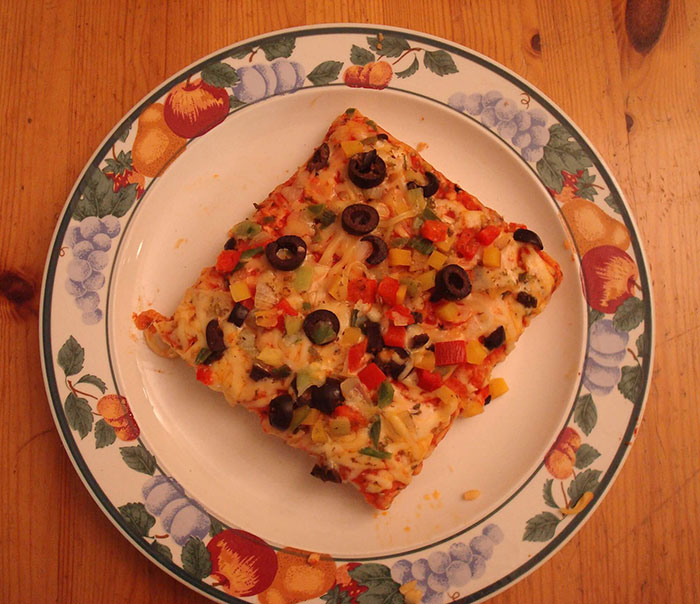 Square pizza slice with olives and peppers on a decorative plate, representing nostalgic 90s foods.