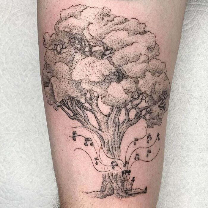 Tattoo of a tree with musical notes flowing around a seated person reflects a unique music tattoo design.