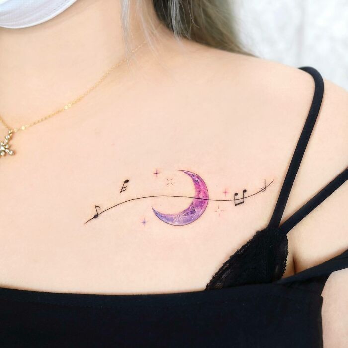 Music tattoo featuring a purple crescent moon with musical notes on a woman's shoulder.