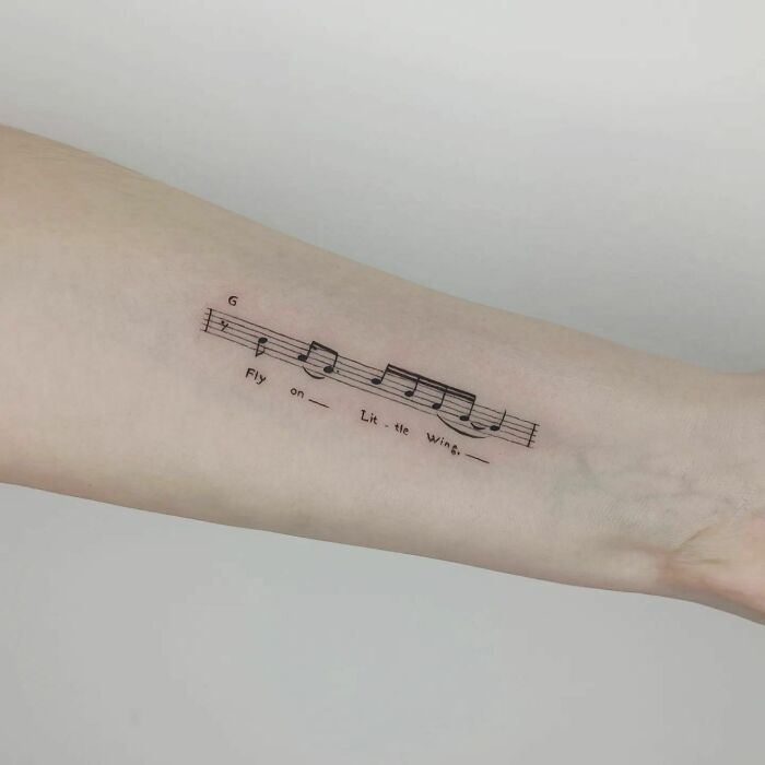 Music tattoo featuring sheet music and lyrics on an arm.