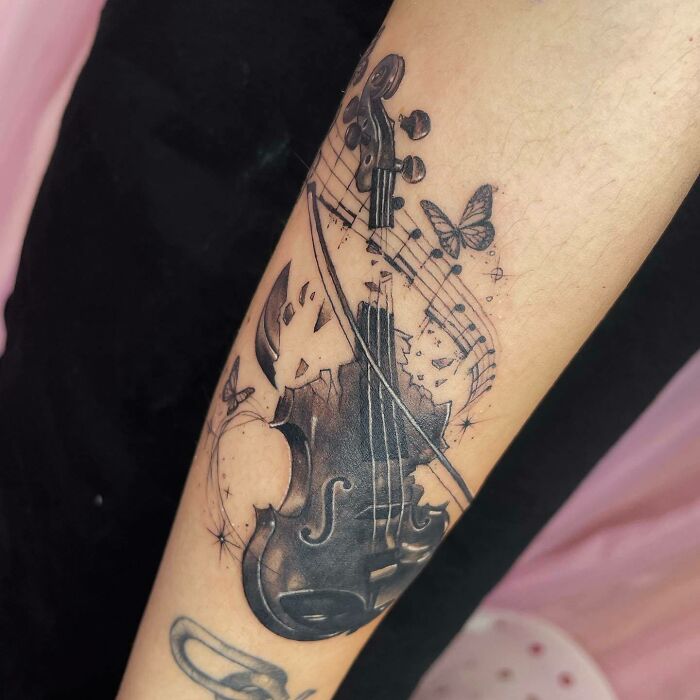 Violin and musical notes tattoo with butterflies on an arm, representing music tattoos.