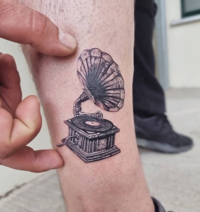 Music tattoo of a vintage gramophone inked on a leg.