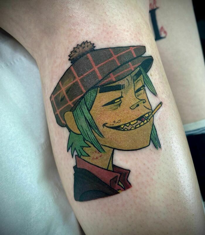 Cartoon character tattoo with a hat and cigarette, showcasing vibrant music-themed ink art.