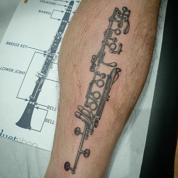 Clarinet music tattoo design inked on a forearm, featuring detailed keys and components.