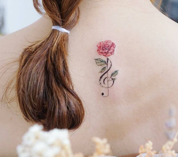 Rose and treble clef music tattoo on a person's back, with long brown hair tied in a ponytail.