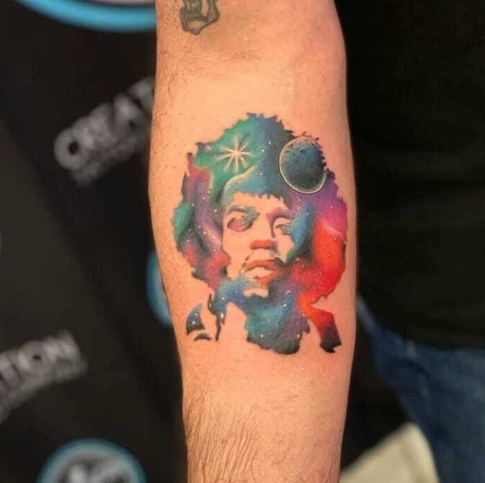 Colorful music tattoo of an iconic musician's face with a cosmic theme on an arm.