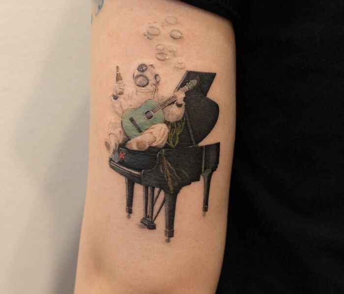 Tattoo of an astronaut playing guitar while sitting on a piano, representing music-themed design.