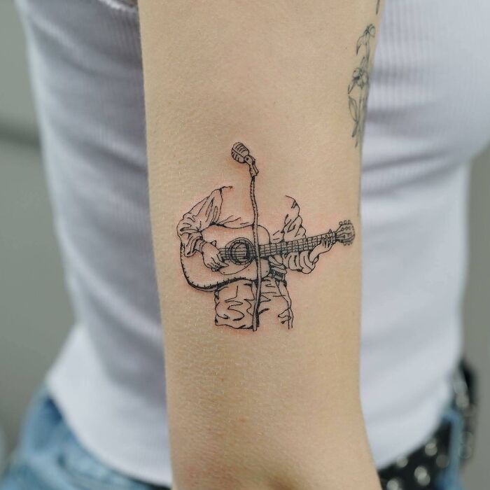 Music tattoo of a guitarist and microphone on an arm, showcasing artistic linework.