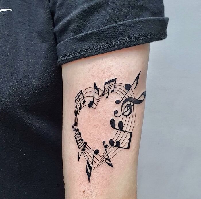 Arm with a music tattoo of a heart made from notes and symbols, showcasing creative music-themed ink design.