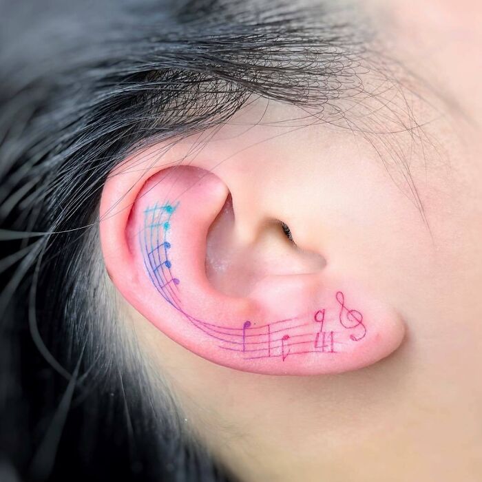 Music tattoo on a person's ear with colorful music notes and symbols.